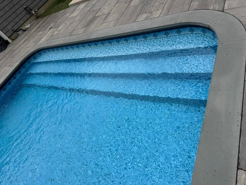 An inground swimming pool with blue water and steps leading into the deep end, bordered by gray stone coping and decking.