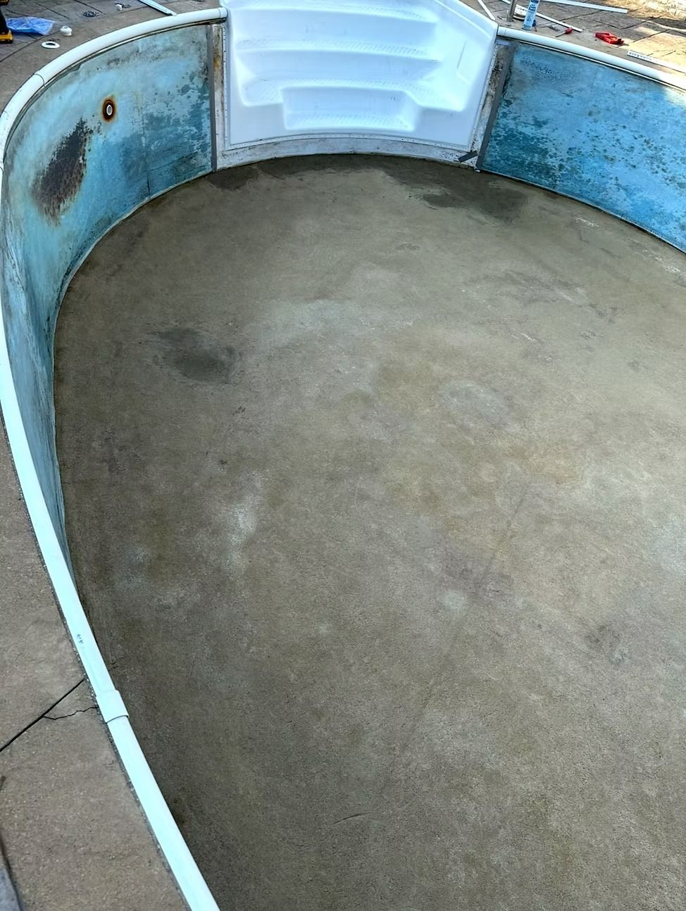 Empty, oval-shaped swimming pool with blue walls and white steps; concrete floor, viewed from above.