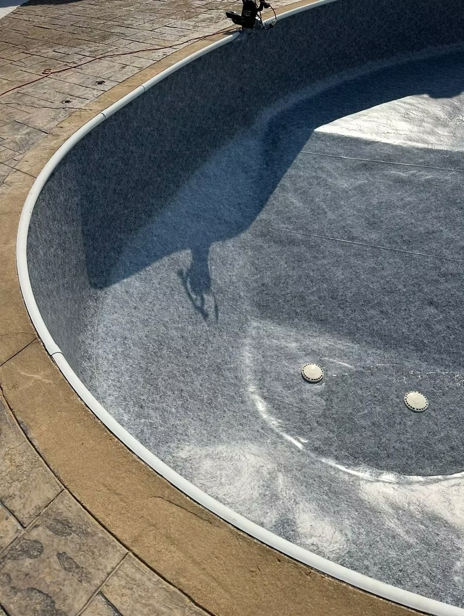 Partially built, oval-shaped swimming pool with blue speckled interior. White coping edge, brown stone surround.