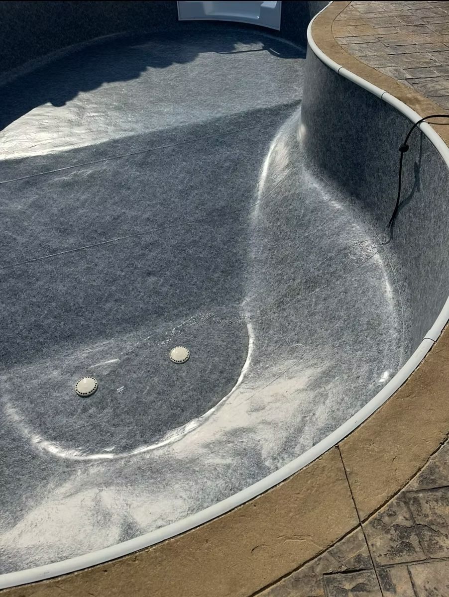 Empty swimming pool with dark gray interior, concrete border, and two circular jets.