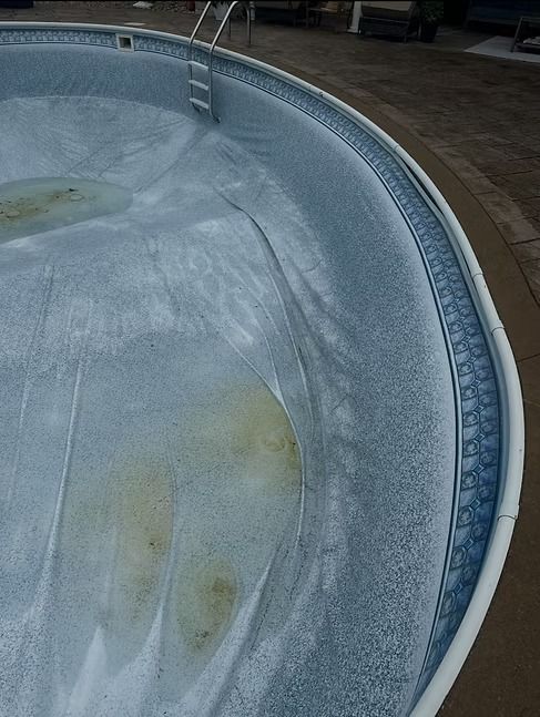 Empty, circular swimming pool with patterned blue interior and white coping; metal ladder.