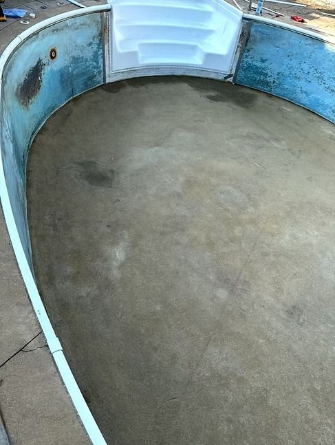 Empty, oval-shaped swimming pool with blue walls, white steps, and a gray concrete floor.
