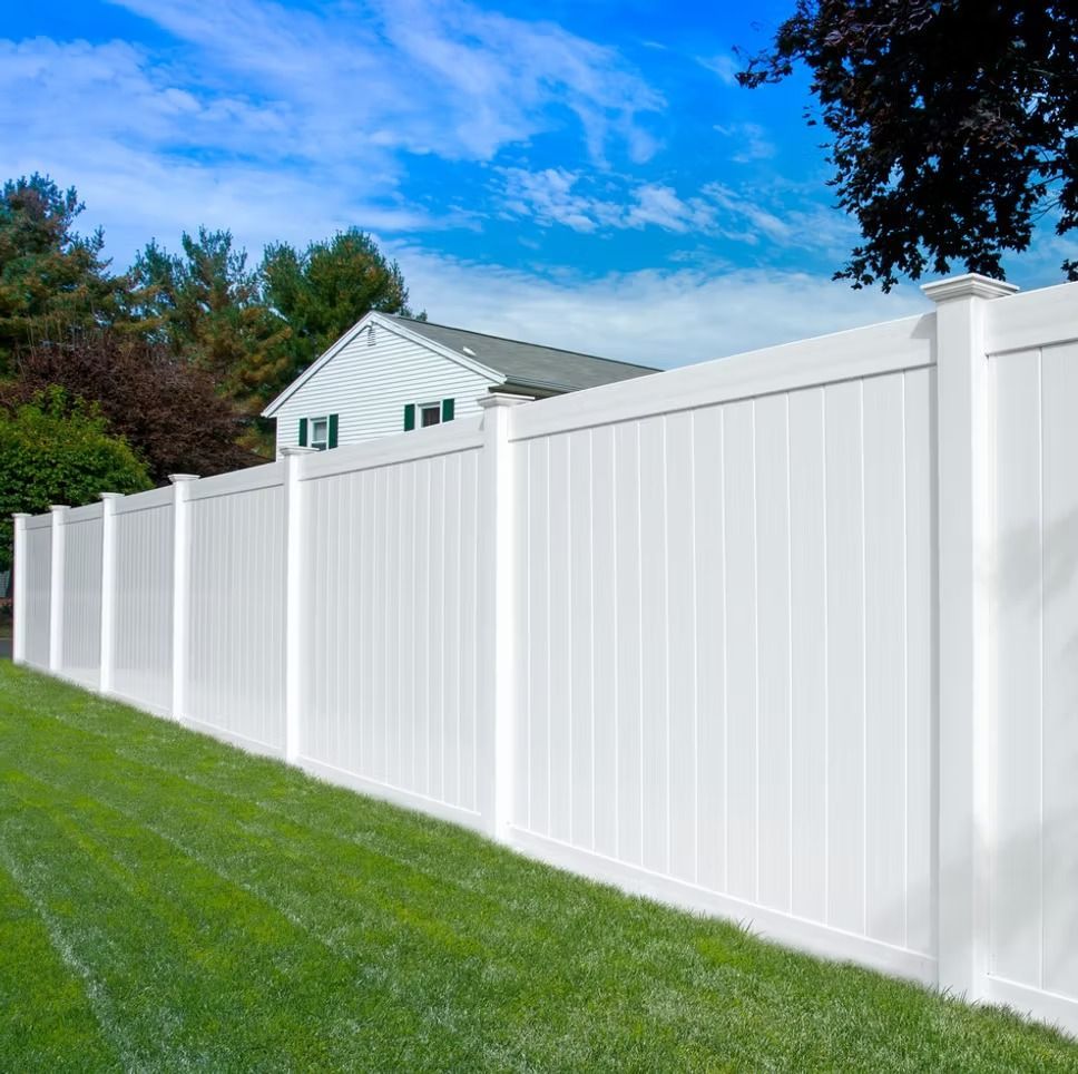 White vinyl privacy fence in a grassy yard, house and trees in the background, against a blue sky.
