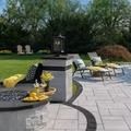 Patio with gray pavers, built-in fire pit, lounge chairs, and manicured lawn.