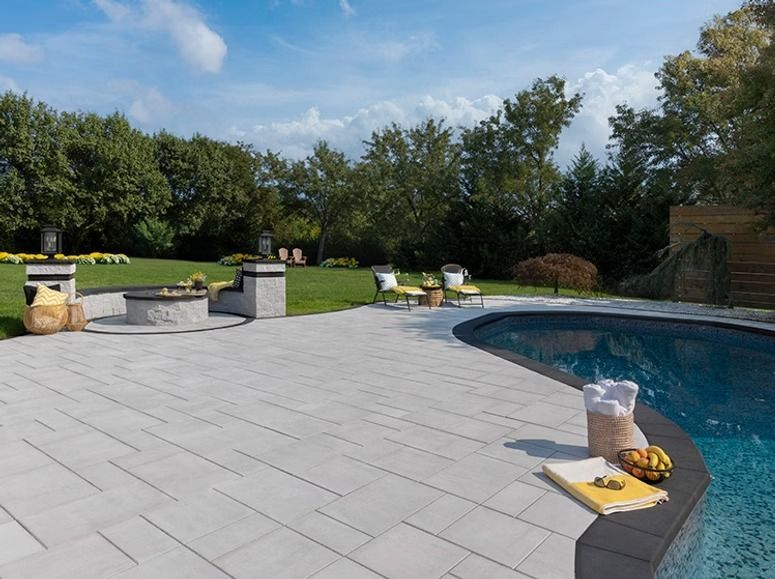 Backyard patio with pool, fire pit, and lounge chairs on a sunny day.