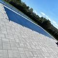 Pool covered with blue tarp, surrounded by light gray paving stones. Blue sky and trees in the background.
