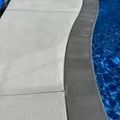 Close-up of a pool's edge, showing gray concrete and blue water.