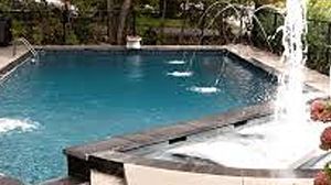 A rectangular swimming pool with integrated water fountains, a spillover spa, and a stone deck in a backyard setting.