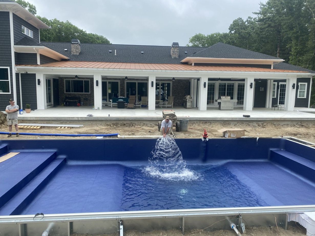 Blue backyard pool with a central fountain in front of a modern house and patio.