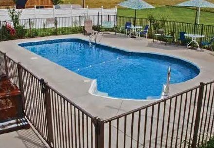 A rectangular backyard swimming pool with a shallow cutout area, surrounded by a metal fence, patio furniture, and lawn.
