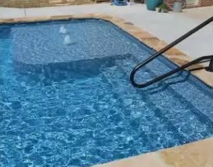Blue pool water with steps, a shallow lounge area featuring two water bubblers, and a black metal handrail.
