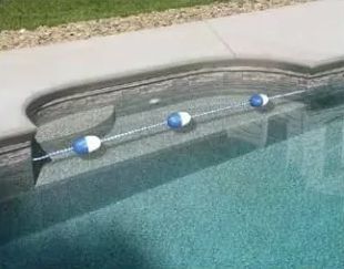 A pool safety rope with blue and white buoys stretched across the shallow end steps of a swimming pool.