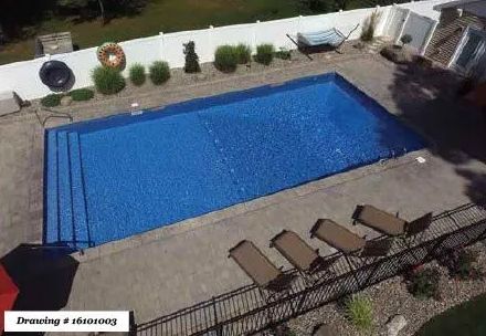 A rectangular swimming pool with blue water and steps, surrounded by a paved patio and four lounge chairs.