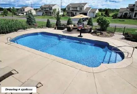 A blue, kidney-shaped in-ground swimming pool on a concrete patio surrounded by a grassy neighborhood landscape.