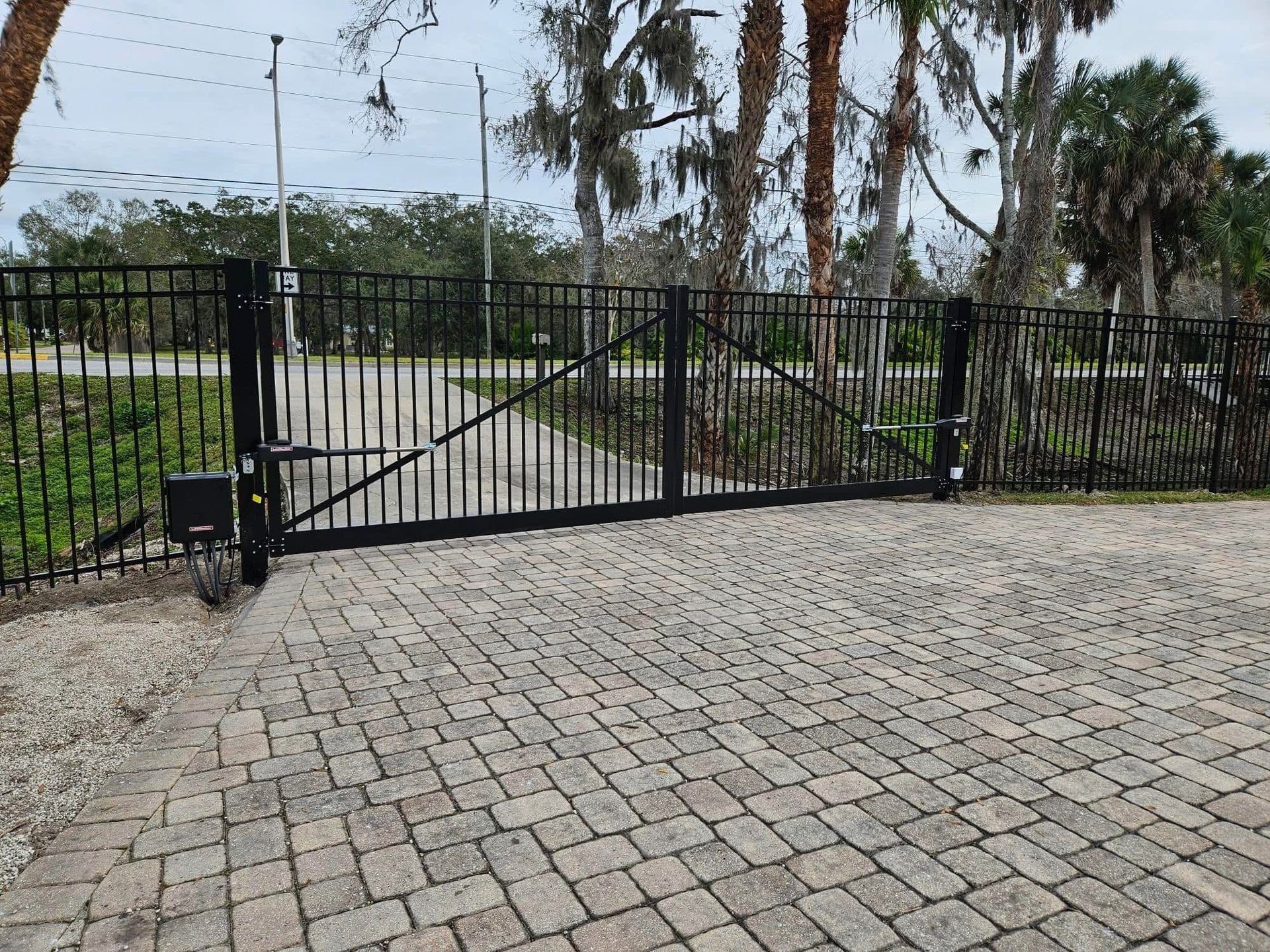 A black gate is sitting on a brick driveway.