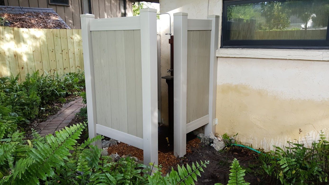 A white shower stall is sitting in the backyard of a house.