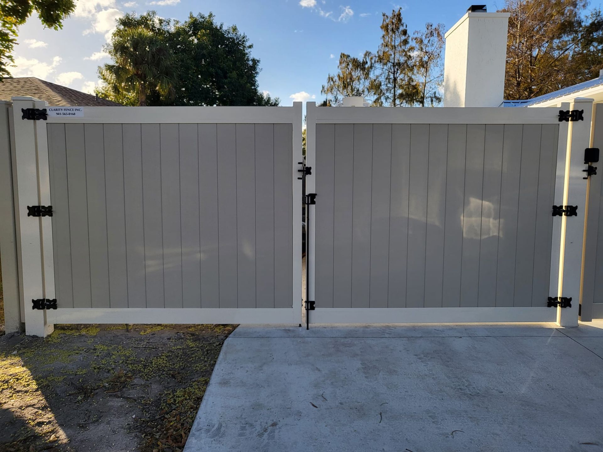 A white fence is sitting on top of a concrete driveway next to a house.