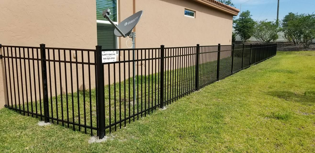 A black metal fence surrounds a grassy yard in front of a house.