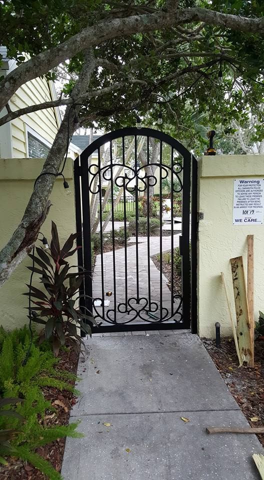 A black wrought iron gate is leading to a sidewalk.