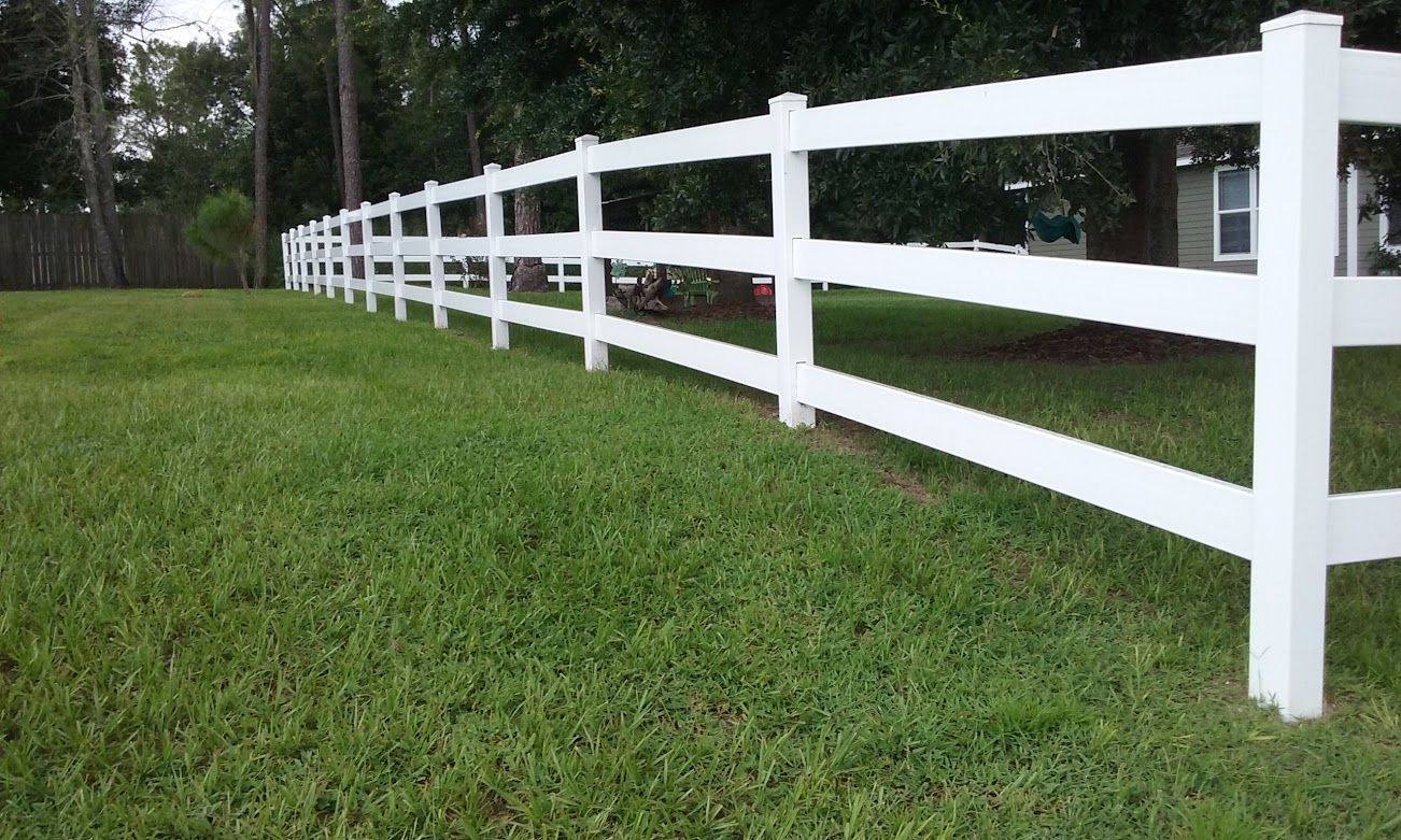 A white fence surrounds a lush green field.