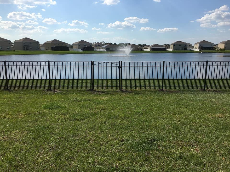 There is a fountain in the middle of the lake behind the fence.
