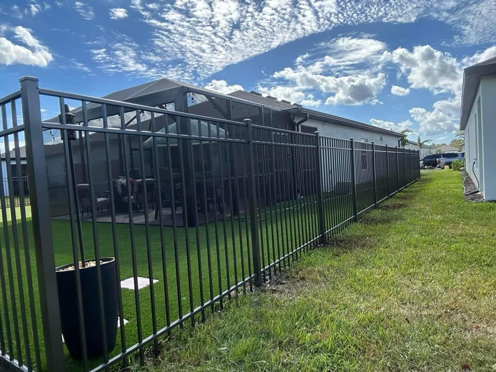 A metal fence surrounds a lush green yard in front of a house.