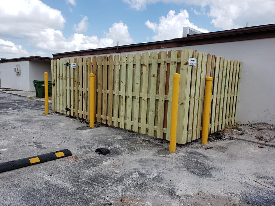 A wooden fence is surrounded by yellow poles in a parking lot.