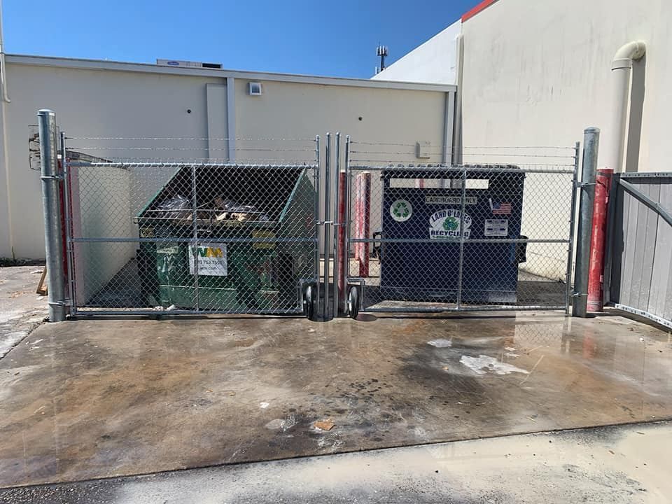 A dumpster and a trash can are behind a chain link fence.