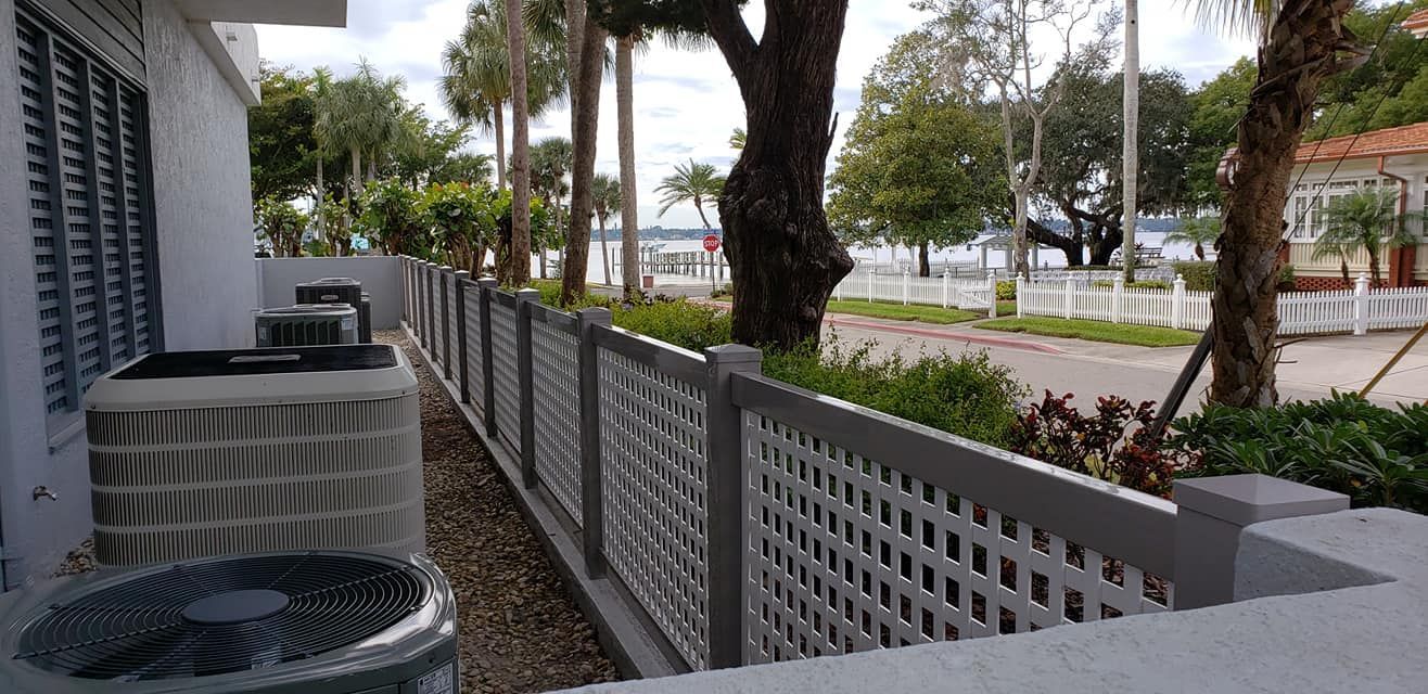 A white lattice fence along the side of a building with trees in the background.