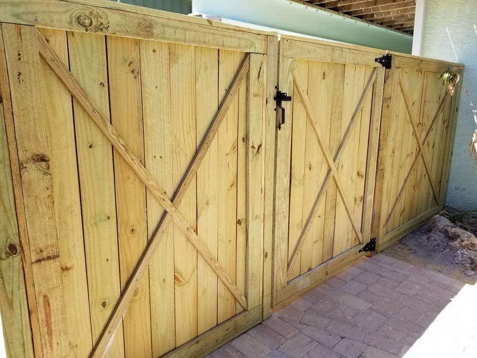 A wooden fence with a gate is sitting on a brick sidewalk.