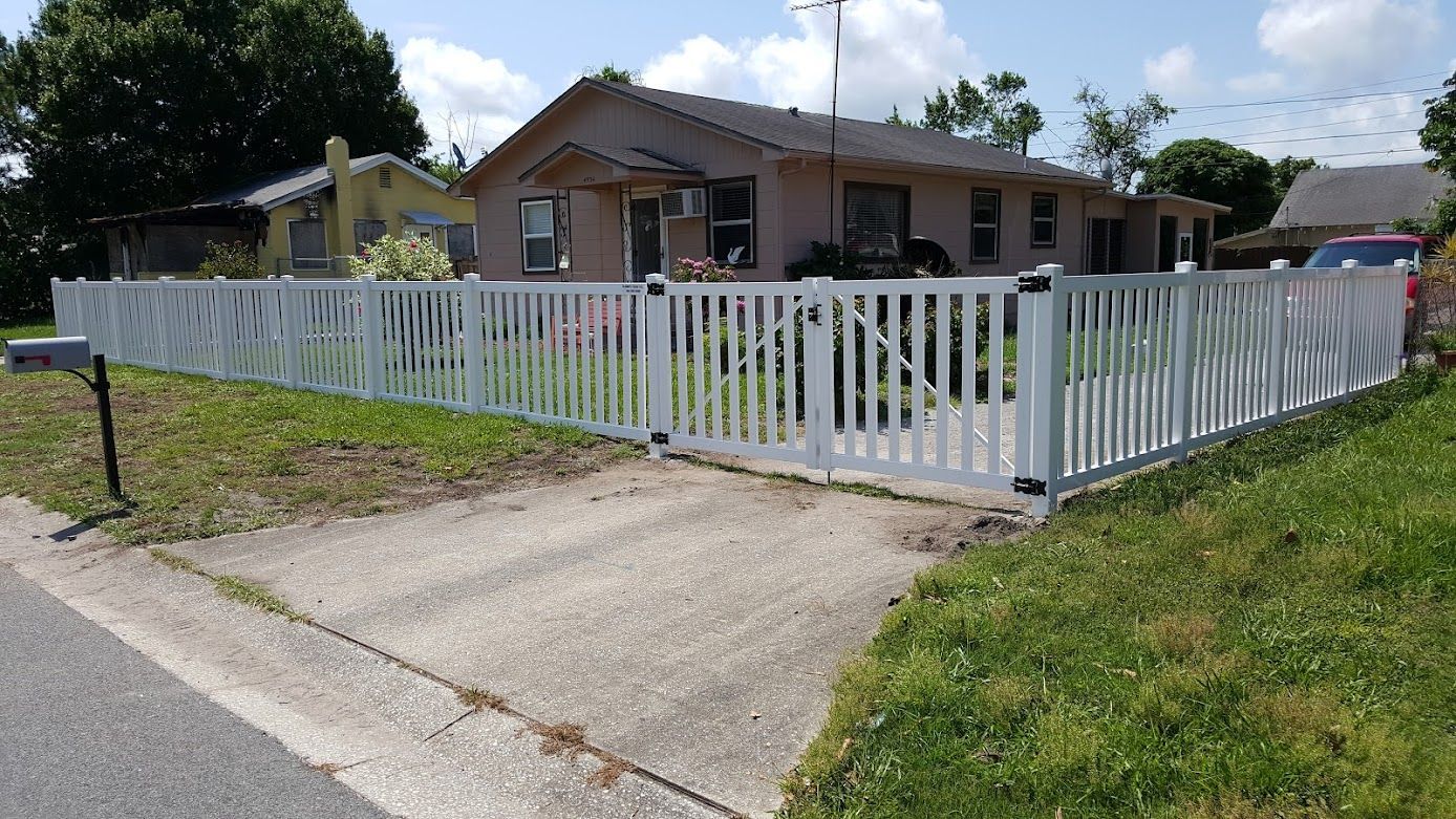 A white picket fence surrounds a driveway in front of a house.