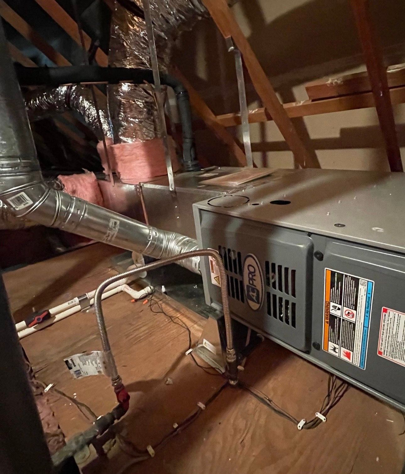 HVAC unit in an attic with ductwork, water pipes, and insulation. Wooden beams and joists are visible.