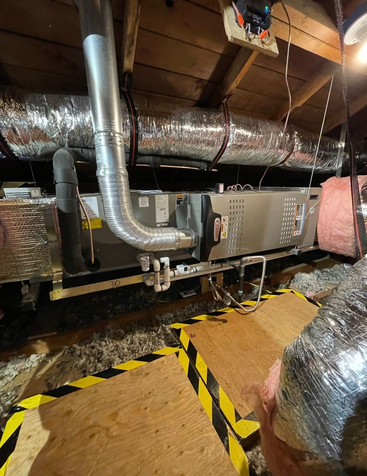 HVAC unit in an attic with ductwork, insulation, and wooden platform for access. Silver and pink colors dominate.