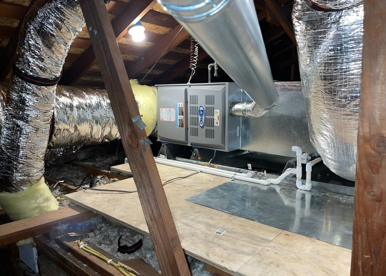 HVAC unit in an attic with ductwork, insulation, and wooden structure.