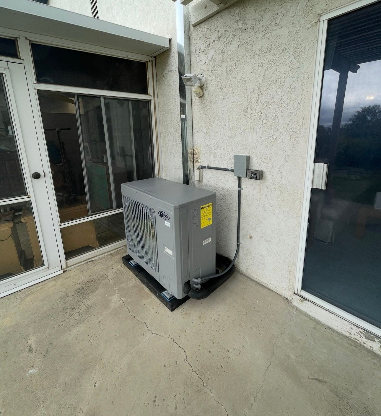 Exterior air conditioning unit on a concrete patio next to a house with sliding glass doors.
