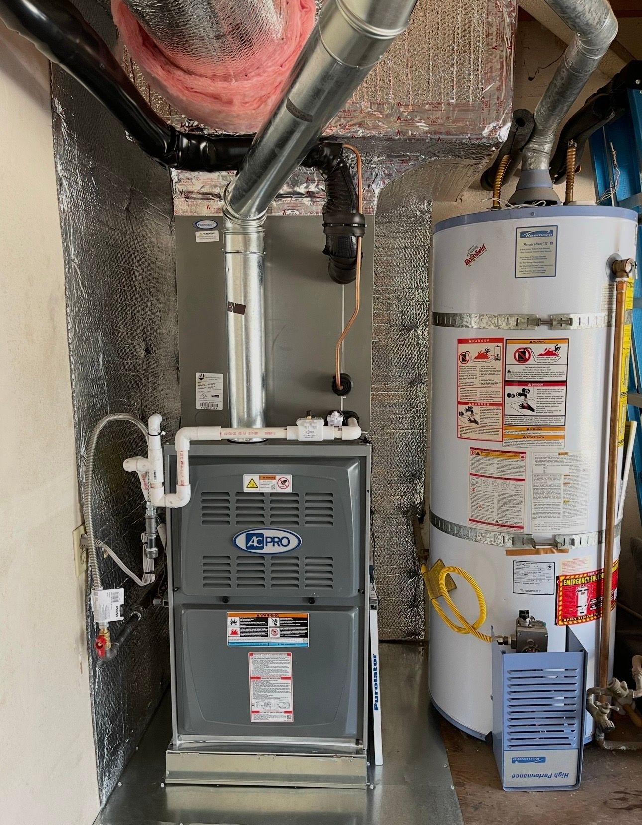 Furnace and water heater in a utility room. Silver ductwork, insulation, and gray furnace with a white water heater.