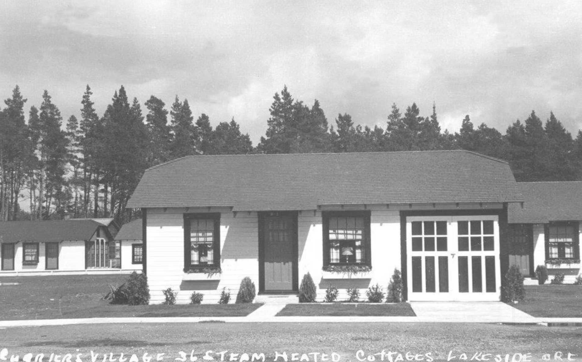 white cottages in a row with garages, surrounded by grass and trees