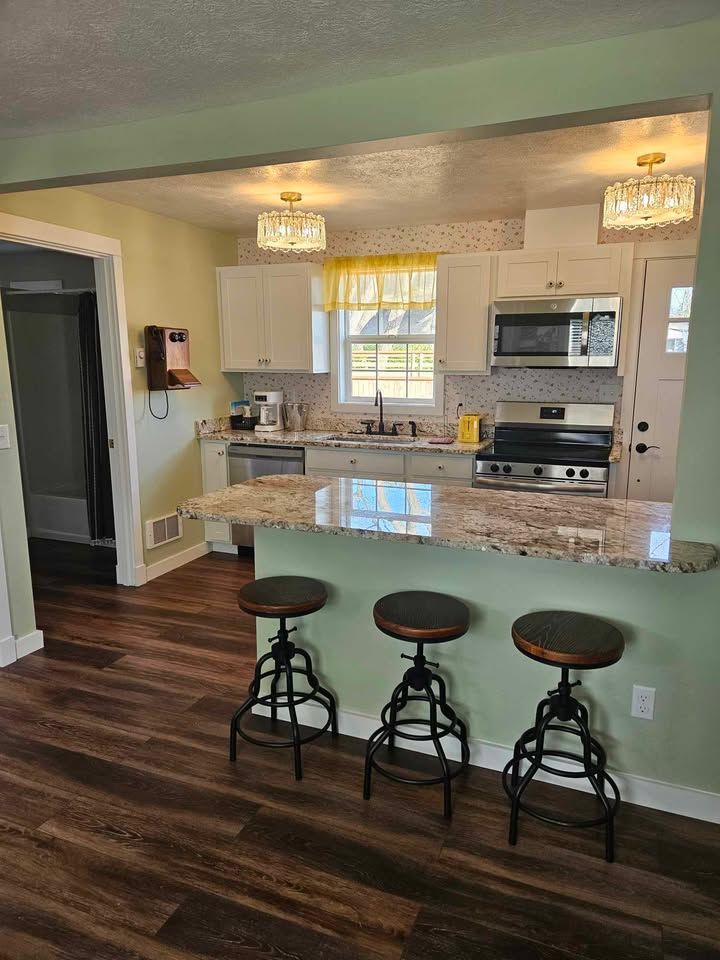Kitchen with bar seating, white cabinets, granite countertops, and pendant lights.