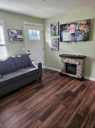 Living room with grey couch, fireplace, TV, and framed art on light green walls.