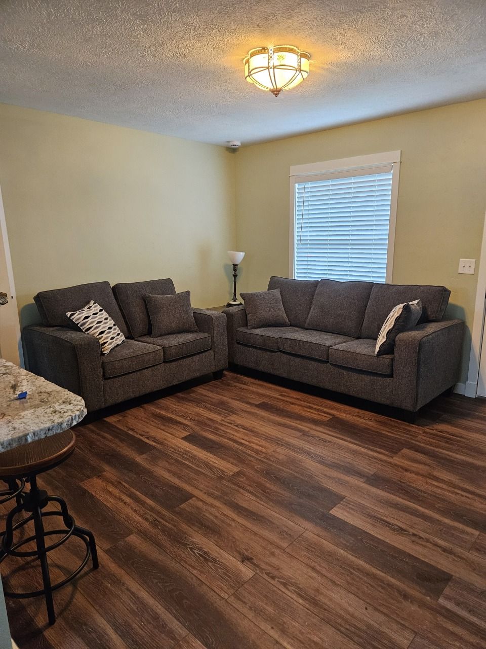 Living room with two gray sofas, wood floors, and a window with blinds.