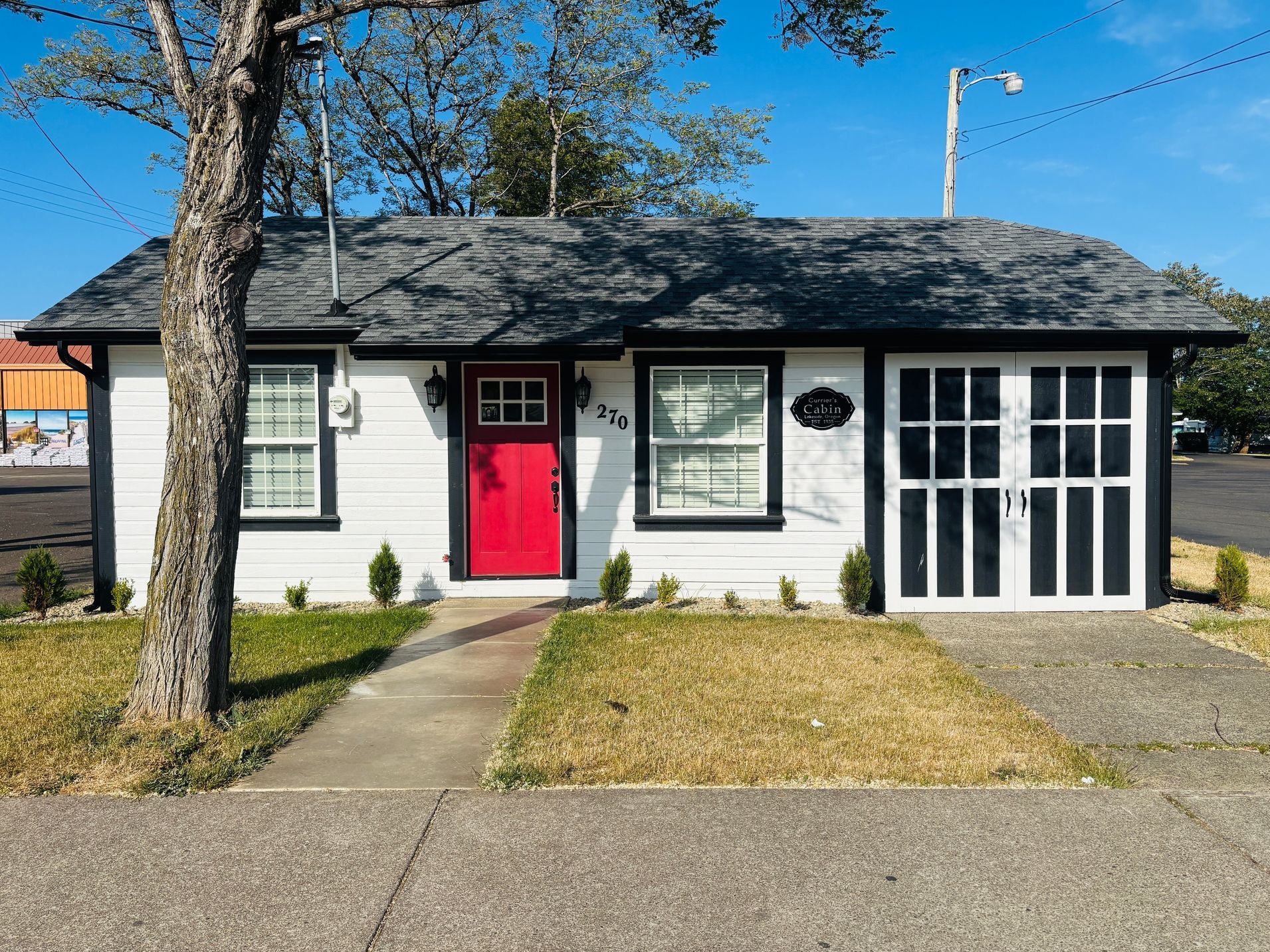 White cottage with a bright red door, black trim, and a garage door.