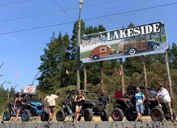 a group of people standing with ATVs in front of a sign