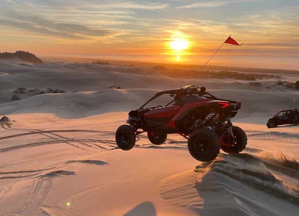 a red off-road vehicle on sand dune at sunset