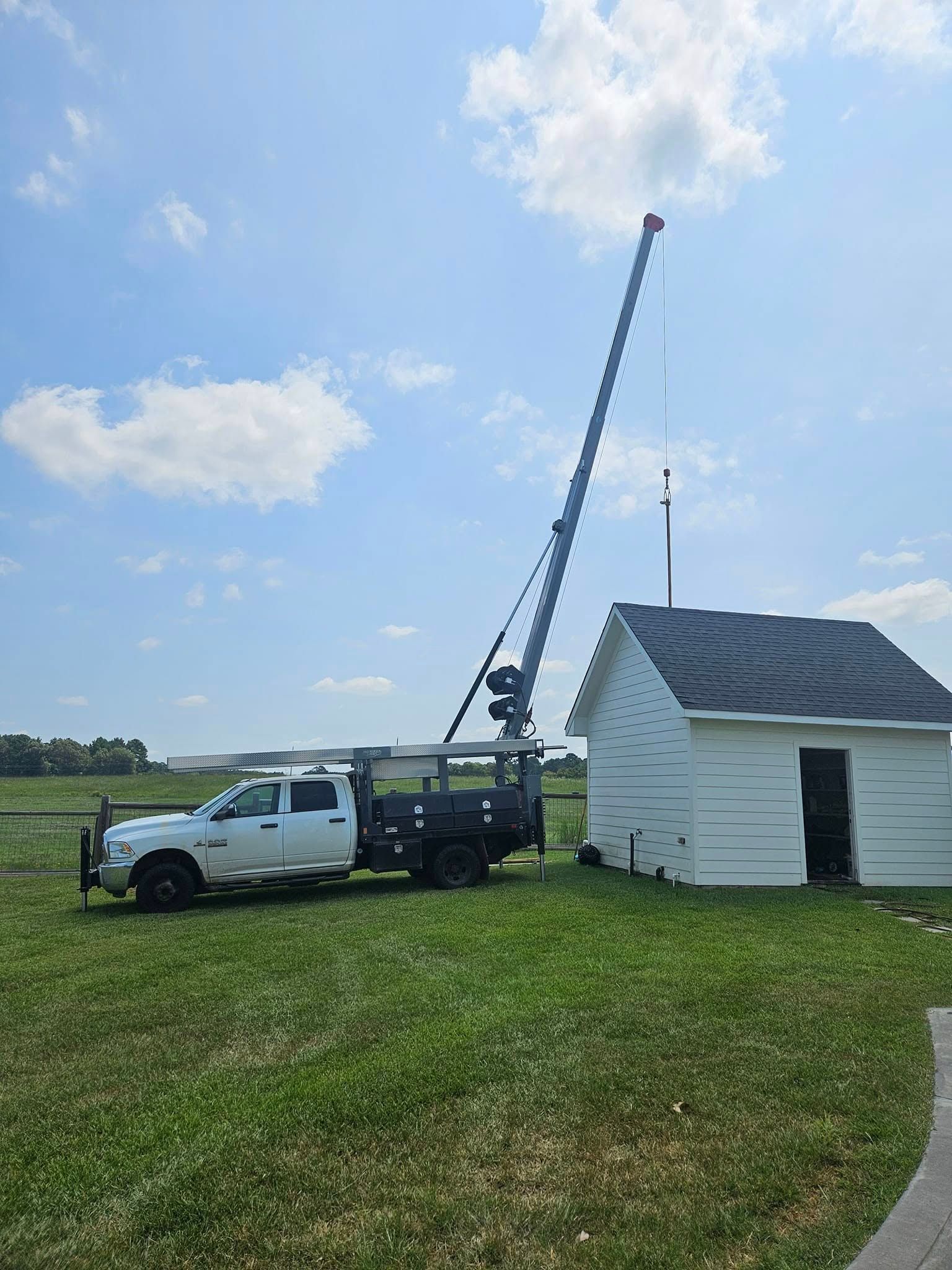 A white truck with a crane is positioned near a small white building on a grassy field.