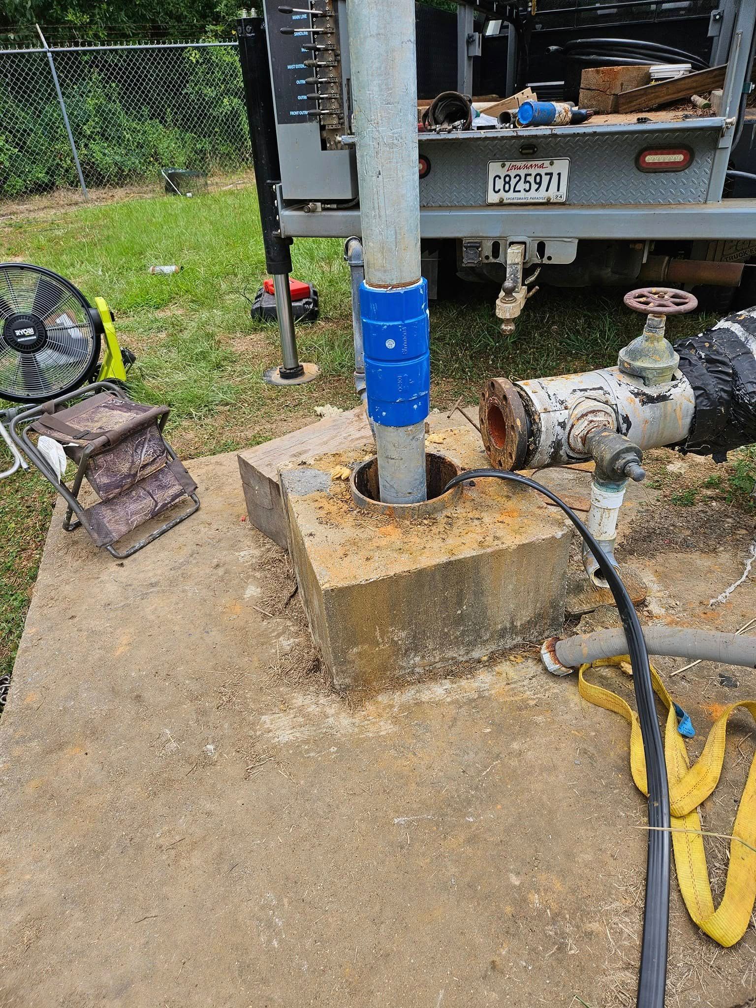 Well with concrete base, rusty valve, and utility truck in the background.