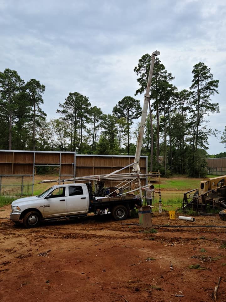 A white truck with drilling equipment, drilling in a field with trees and a cloudy sky in the background.