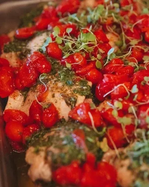 Baked fish topped with vibrant red cherry tomatoes, green pesto, and microgreens.