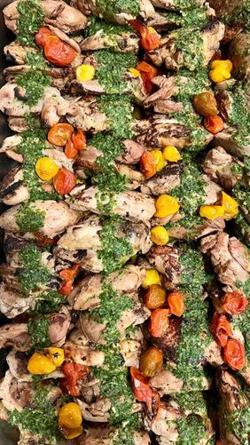 Grilled chicken topped with green herbs and roasted red and yellow tomatoes in a tray.