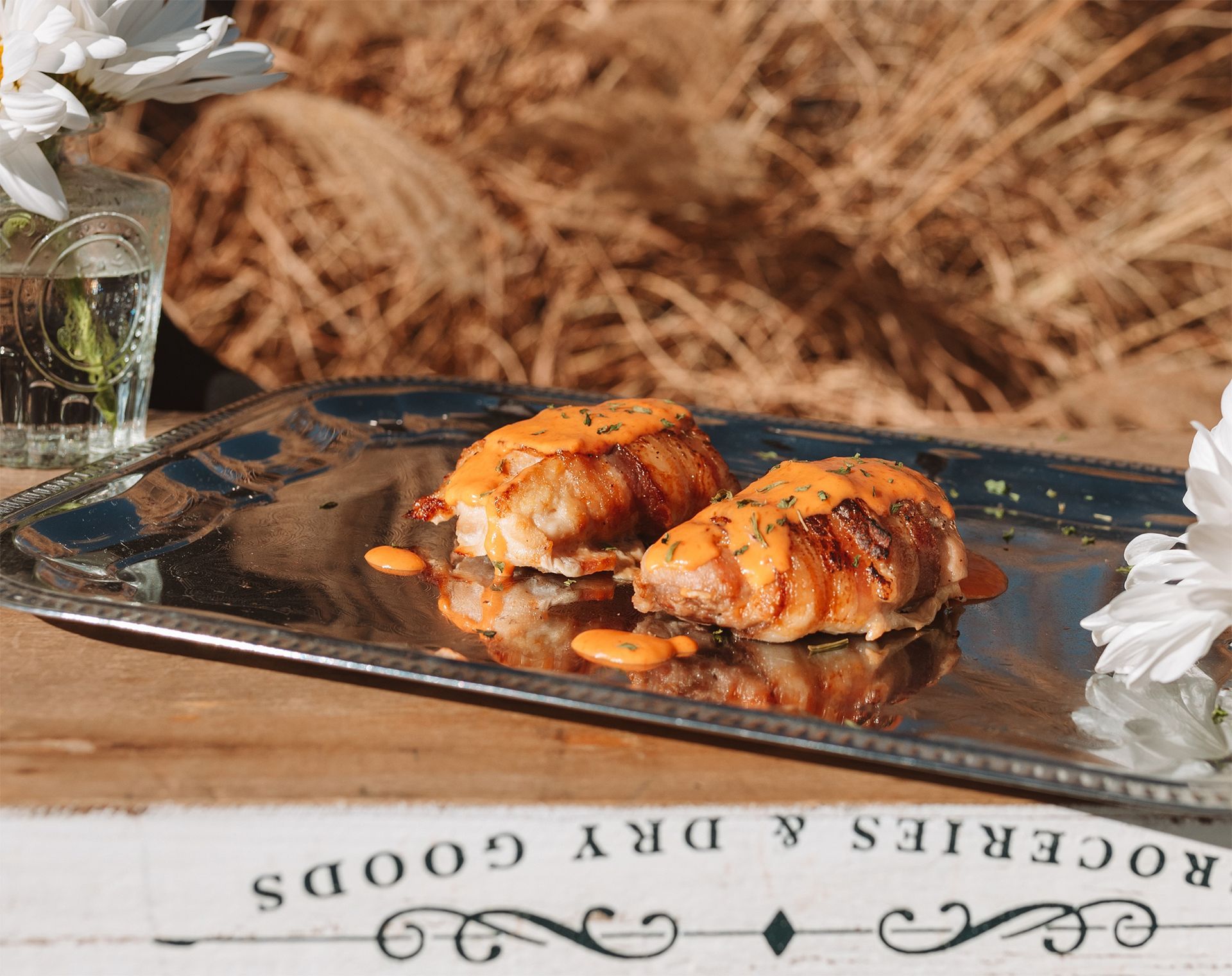 Two potato stacks with sauce on a silver tray outdoors, near flowers.