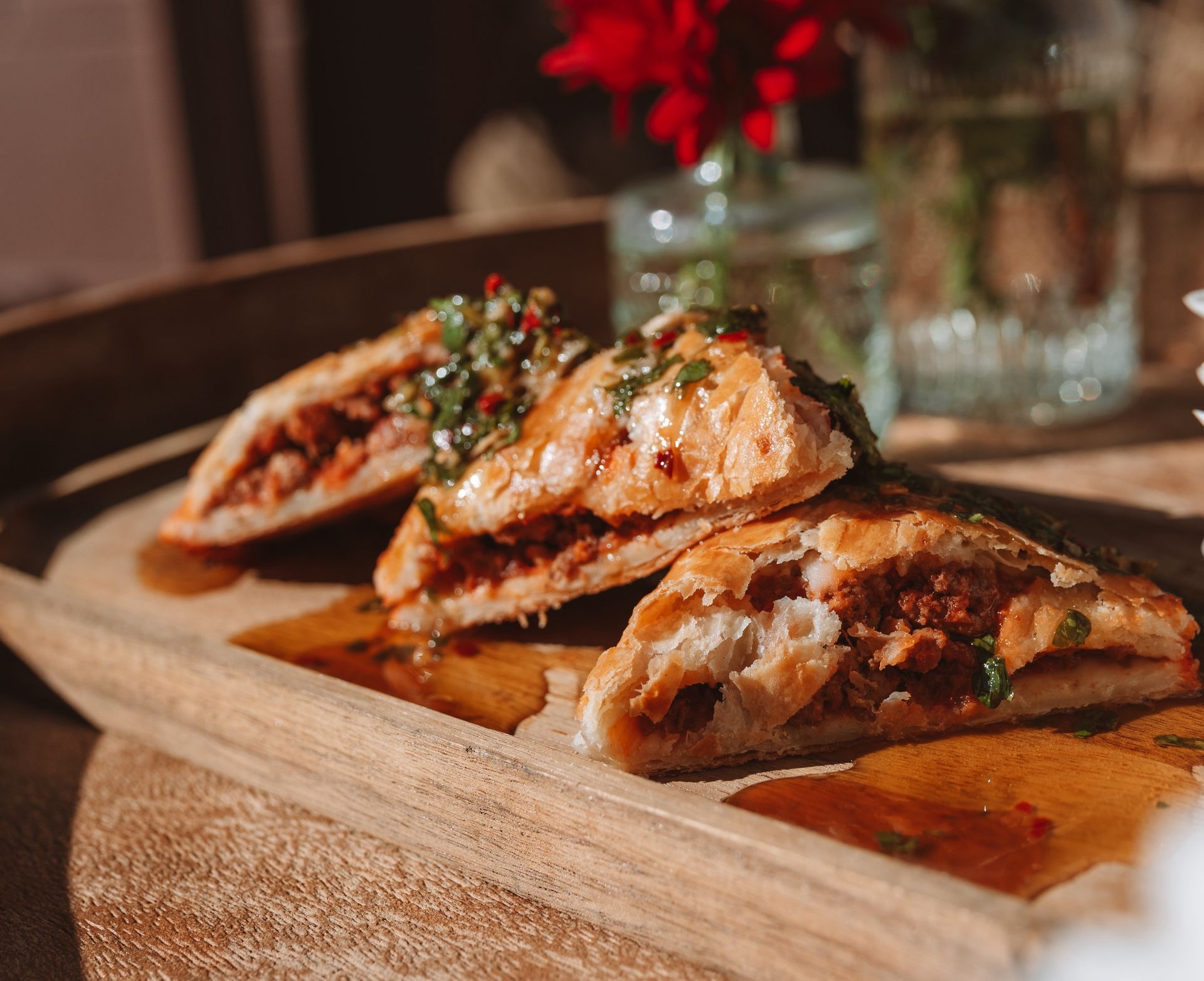 Savory pastries with meat filling on a wooden board, topped with sauce and herbs.